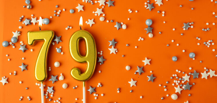 Birthday or anniversary celebration concept. Candles in the shape of the number seventy-nine on an orange background among decorative ornaments. 79th anniversary. Banner