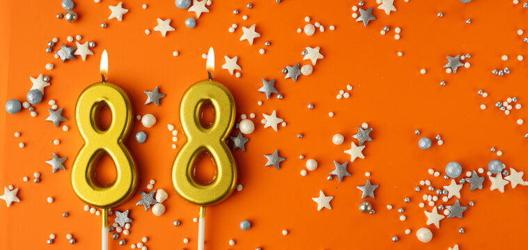 Birthday or anniversary celebration concept. Candles in the shape of the number eighty-eight on an orange background among decorative ornaments. 88th anniversary. Banner