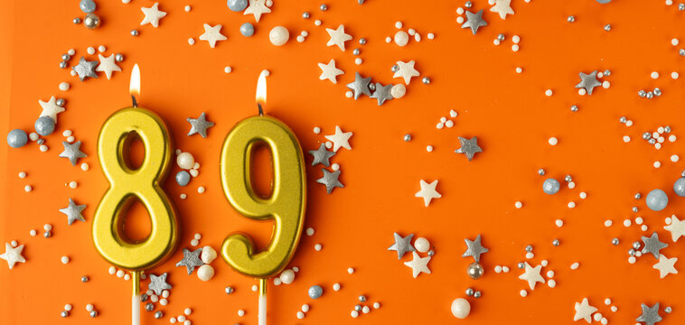 Birthday or anniversary celebration concept. Candles in the shape of the number eighty-nine on an orange background among decorative ornaments. 89th anniversary. Banner