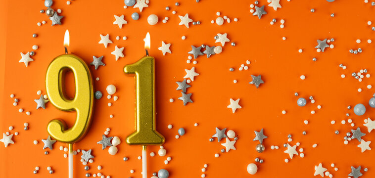 Birthday or anniversary celebration concept. Candles in the shape of the number ninety-one on an orange background among decorative ornaments. 91st anniversary. Banner