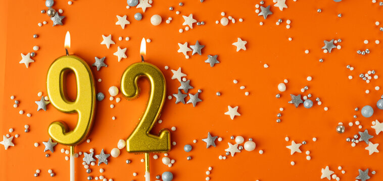 Birthday or anniversary celebration concept. Candles in the shape of the number ninety-two on an orange background among decorative ornaments. 92nd anniversary. Banner