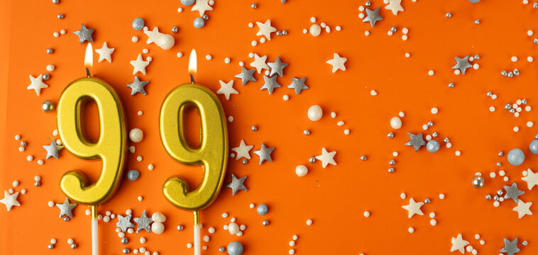 Birthday or anniversary celebration concept. Candles in the shape of the number ninety-nine on an orange background among decorative ornaments. 99th anniversary. Banner