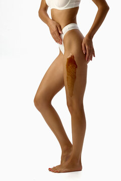 Standing woman showing wax strip to upper thigh. Concept of thigh waxing, professional epilation, beauty treatment, beauty service, waxing products.