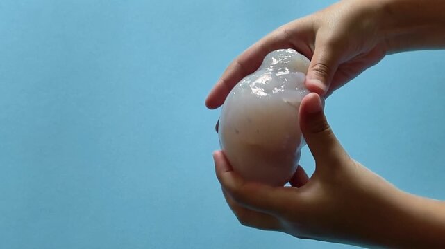 Child's hands stretching, squeezing, and playing with clear glitter slime against a solid blue background, demonstrating sensory and tactile play for stress relief