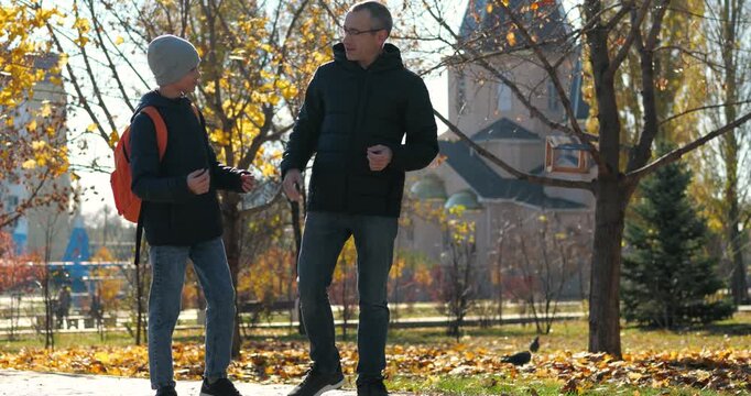 Father and son walk through autumn park, happily talking and sharing a joyful moment. Father embraces his son as they continue walking together, highlighting family bonding, affection and quality time