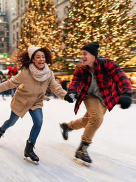 Happy Young Couple Ice Skating Together Outdoors near Illuminated Christmas Tree