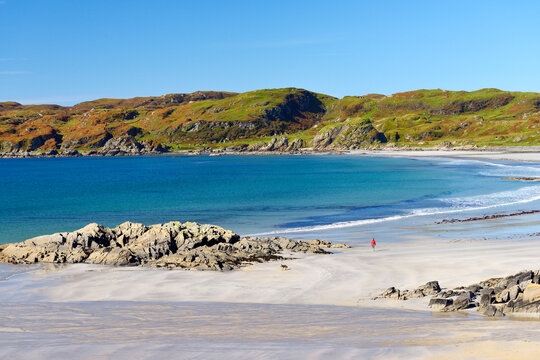 Sanna beach on Ardnamurchan peninsula on west coast of Scotland. Woman walking dog on deserted unspoilt white sand in the western Scottish Highlands