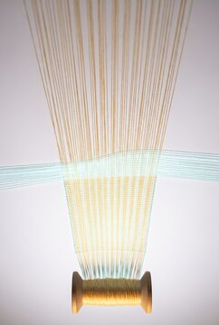 Golden threads weave across a 3D wooden spool
