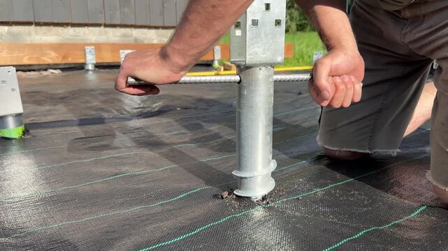 Worker preparing and screwing ground screw before building a wooden terrace foundation, construction preparation, site leveling, home improvement, outdoor renovation, manual work.
