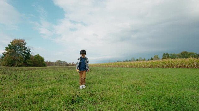 Asian Boy Walking Across Grassy Field Holding Ear of Corn
