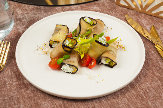 Grilled eggplant rolls stuffed with cream cheese, herbs, cherry tomatoes, and microgreens on white plate