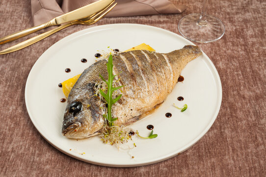 Whole roasted sea bream fish with balsamic glaze drops and microgreens on white plate