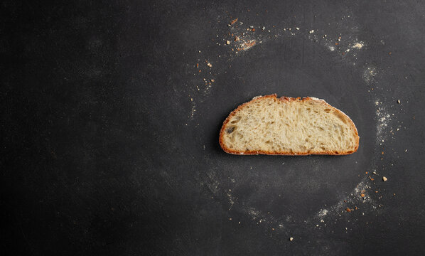 Slice of freshly baked bread placed on a dark textured surface with flour scattered around, showcasing a rustic kitchen setting ideal for culinary photography. copy space