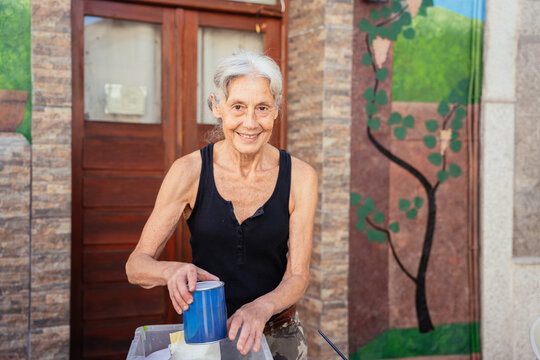 Smiling Senior Woman Preparing Painting Supplies Outdoors in Traditional Spanish Town Setting