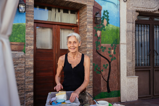 Senior Woman with Art Supplies Preparing for Outdoor Painting Project in Spanish Town