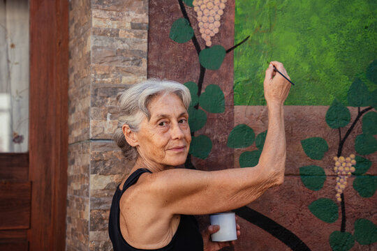Portrait of Senior Female Artist Painting Colorful Grape Vine Mural on Exterior Wall in Spain