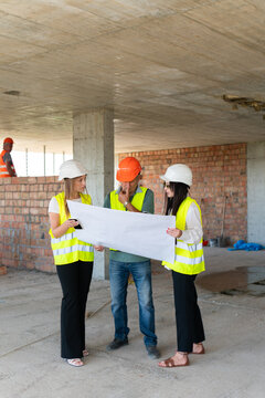 Builder shows floor plan of building to female project managers. Contractor explains document and technical details standing against brick walls