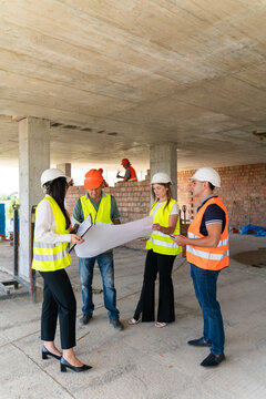 Project managers and builders study large floor plan. Female engineer holds clipboard and talks to colleagues discussing work process