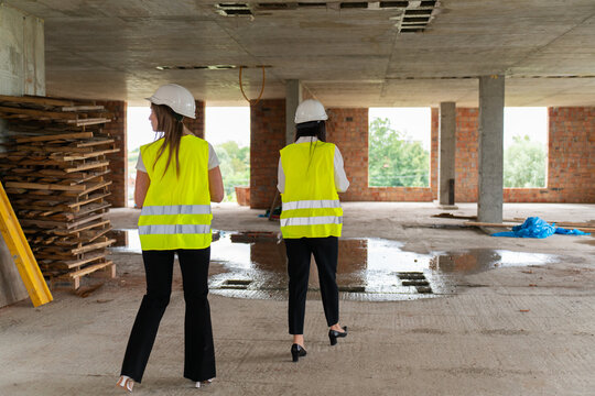 Female engineers inspect work areas during verification process. Women in hard hats and vests analyze results of building assessing project stage