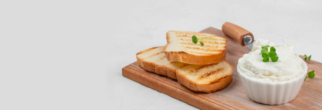 Slices of grilled bread served on a wooden cutting board alongside a bowl of creamy cheese spread garnished with fresh herbs and a cheese knife. copy space
