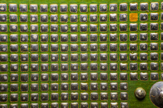 Close-up view of a green circuit board featuring numerous metallic pins and components arranged in a grid pattern, showcasing intricate electronic design and engineering