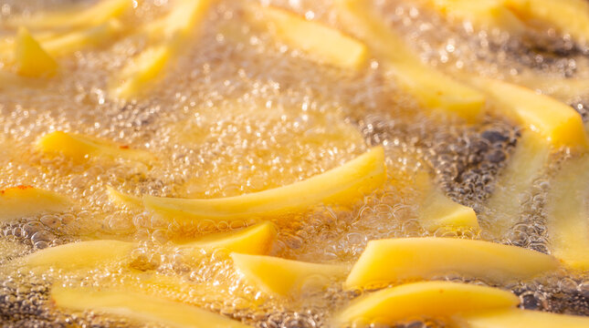 Freshly cut potato strips frying in hot oil, creating bubbles and a golden texture, captured in a close-up view of the cooking process