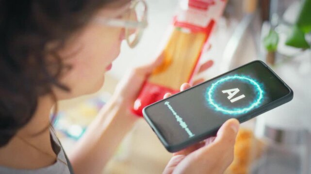 In the kitchen a woman communicates with an AI assistant on her smartphone holding a pasta package. Concept of modern technology, smart home and AI helping with daily cooking routine