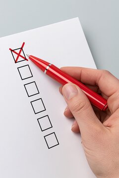 Close up of hand hold red pen and mark cross on checklist paper sheet