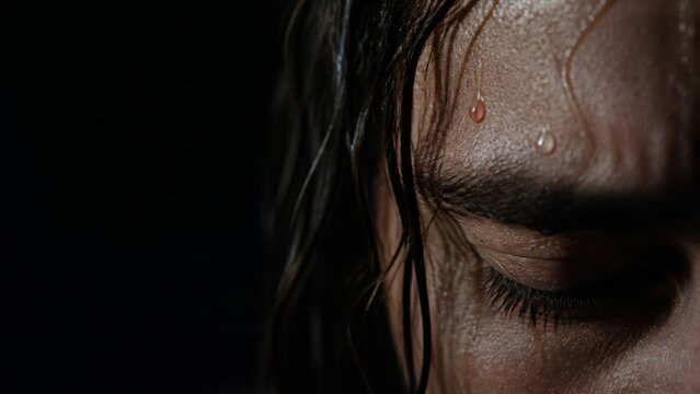 Man with closed eyes and sweat drops like blood on face in darkness. Jesus praying in agony in garden of Gethsemane. Biblical scene of passion and suffering of Christ before crucifixion.