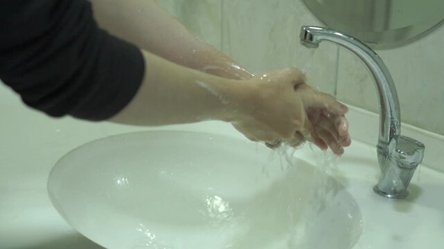Rinsing Soapy Hands Under Running Tap Water in Bathroom Sink