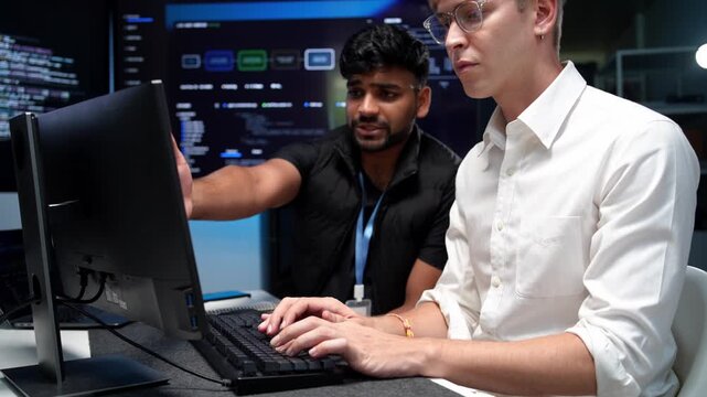 Two colleagues working together on a computer in a contemporary office space with programming code displayed on the monitor
