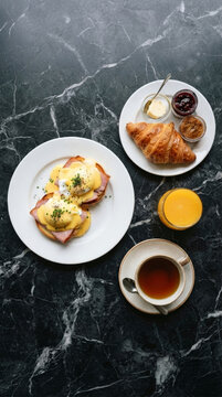 Delicious gourmet breakfast with Eggs Benedict, a croissant, a cup of tea, and fresh orange juice.