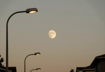 Obraz premium Evening atmosphere and urban twilight, full moon rising over suburban neighborhood with glowing street lights in a calm dusk sky for peaceful mood