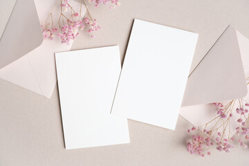 Blank white stationery cards with pink envelopes and dried flowers arranged on a soft beige background for invitations or greeting cards © nikavera