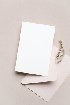 Blank white card placed on a soft beige background next to a light pink envelope and dried flowers, suitable for invitations or greeting cards