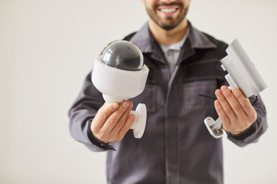 Cropped shot of smiling technician standing against gray wall and presenting security cameras. Installer showing assembly parts for surveillance system setup. Surveillance system, CCTV and privacy