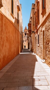 Sunlit narrow alley with warm stone walls and distant church tower