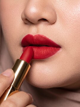 Close up view of a woman carefully applying bold red lipstick to her lips with a golden cosmetic tube, highlighting beauty and makeup.