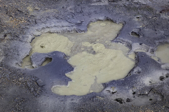 View of bubbling mud pots at Seltun Geothermal Area with grey volcanic soil and steaming mineral deposits in Grindavik, Hafnarfjardarkaupstad, Iceland.