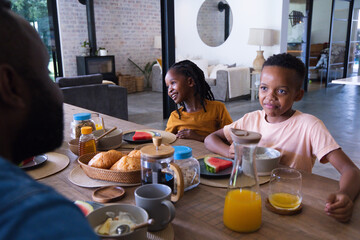 Naklejka premium African American family sharing breakfast at wood table at home children in mustard and pink shirts