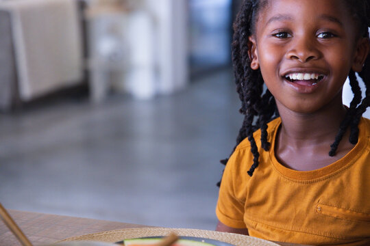 African American child sitting smiling at table wearing mustard tee with plate placemat, copy space