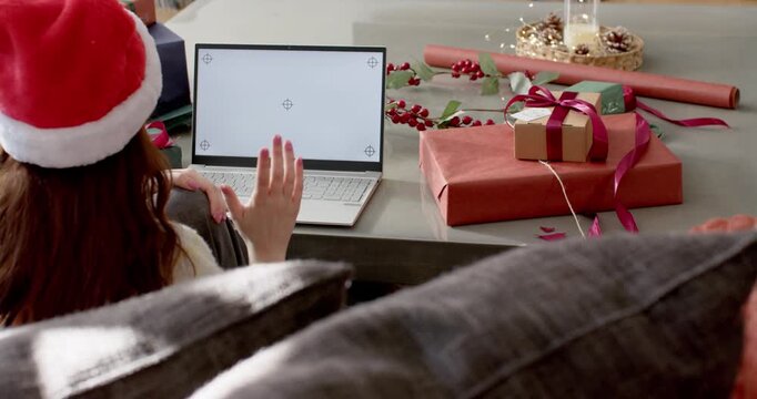 Noticing blank laptop screen, girl is waving hand at low table with gifts for holiday call