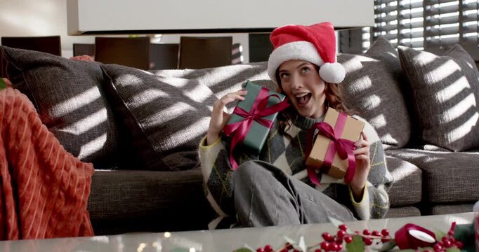 Woman wearing Santa hat on couch holding wrapped gifts raising green glancing aside smiling festive