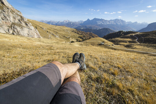 View of a hiker resting on a grassy mountain slope with boots visible, looking towards the Peitlerkofel peak in the Dolomites, Brixen, Trentino-Alto Adige, Italy.