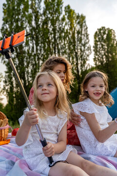 Mother and young daughters enjoying a picnic, taking a selfie with a smartphone and monopod