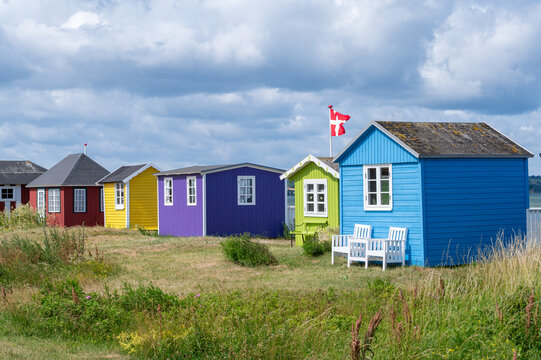 Farbenfrohe Strandh&auml;user in Blau, Gr&uuml;n, Violett, Gelb und Rot stehen an der d&auml;nischen K&uuml;ste (&AElig;r&oslash;sk&oslash;bing) unter einem dramatisch bew&ouml;lkten Himmel.
