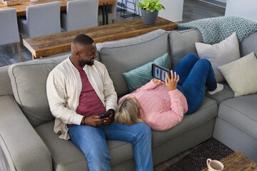 Couple on gray sofa African American man sitting holding phone woman in pink sweater viewing tablet
