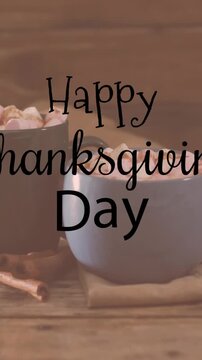Animation of happy thanksgiving day text over mugs with hot chocolate on wooden background