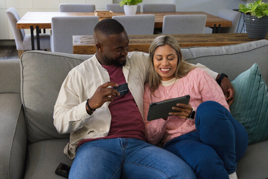 African American couple sitting closely on light-gray sofa at home, holding tablet and credit card