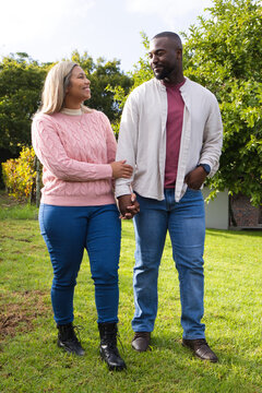 African American couple walking across backyard lawn holding hands, wearing pink sweater